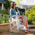 Woman sits comfortably in a floral Freestyle Rocker, enjoying a snack in a sunny garden.
