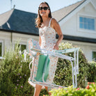 Smiling woman in a floral dress carries a folded Freestyle Rocker through a vibrant garden.