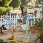 Woman in a jean jacket smiles while sitting in a floral Freestyle Rocker at a sunny garden party.