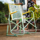 Close-up of an empty floral Freestyle Rocker chair on a garden path near greenery.