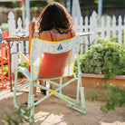 Back view of a woman sitting in the Freestyle Rocker, enjoying a meal at a backyard garden table.