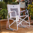 Pink and white floral Freestyle Rocker with mesh back and drink holder sits on a garden path.