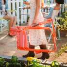 Woman in a white dress carries a folded orange floral Freestyle Rocker while holding a green drink.