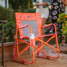 Freestyle Rocker in orange floral print sits near a garden bed with a tumbler in the drink holder.