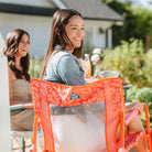 Woman in a white dress and denim jacket smiles while seated in a vibrant orange Freestyle Rocker.