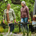 A man and woman smile while carrying folded indigo Freestyle Rocker chairs near a parked vehicle in a forest setting.