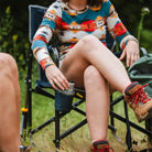 A woman in hiking boots places a drink into the cupholder of a navy Freestyle Rocker while sitting outdoors.