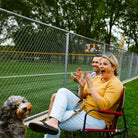 Woman cheering at a sports game while sitting on a cinnamon Freestyle Rocker with a dog beside her.