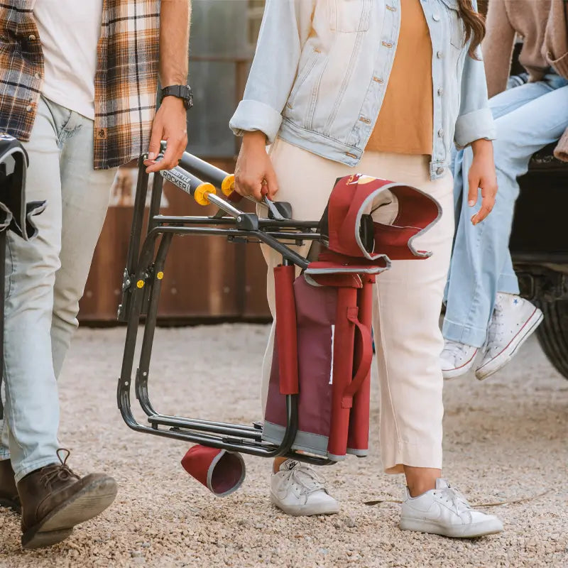 Person carrying a folded cinnamon Freestyle Rocker by the handle for easy transport.