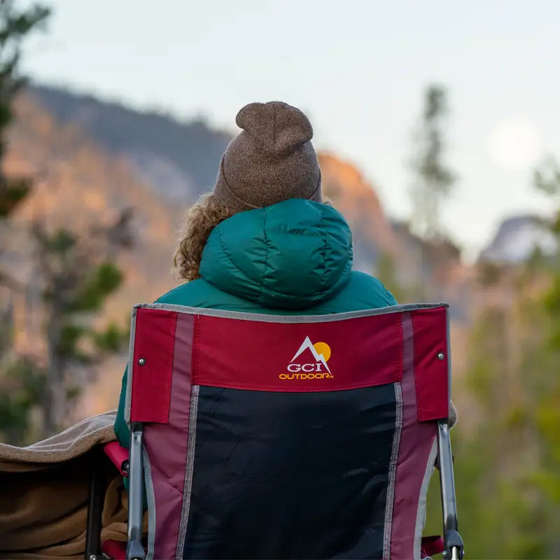 Back view of someone bundled up in the cinnamon Freestyle Rocker, overlooking a scenic mountain landscape.