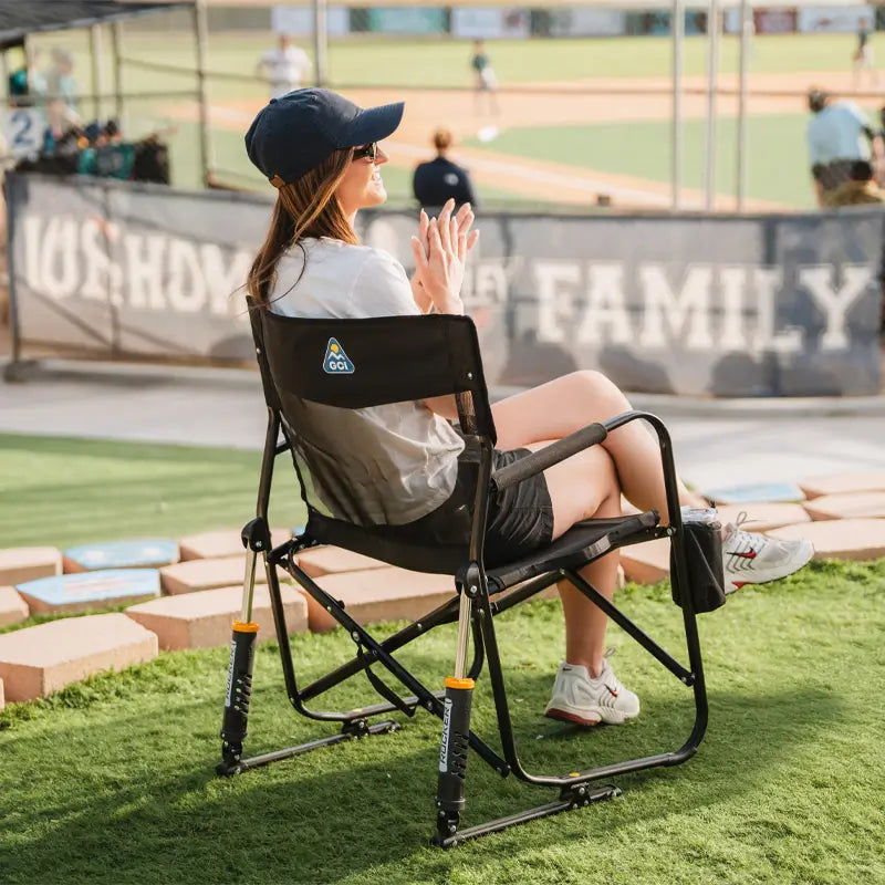 Woman claps while seated in a Black Freestyle Rocker Elite chair at a baseball game.