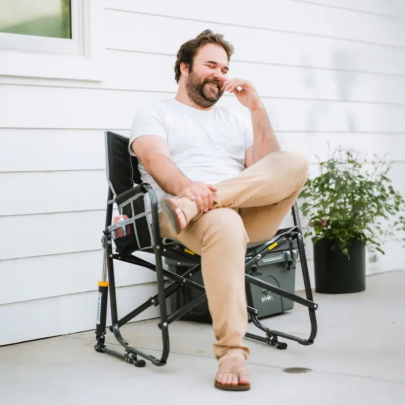 Man smiling and relaxing on a porch in a black Freestyle Rocker XL, seated with legs crossed in a casual setting.
