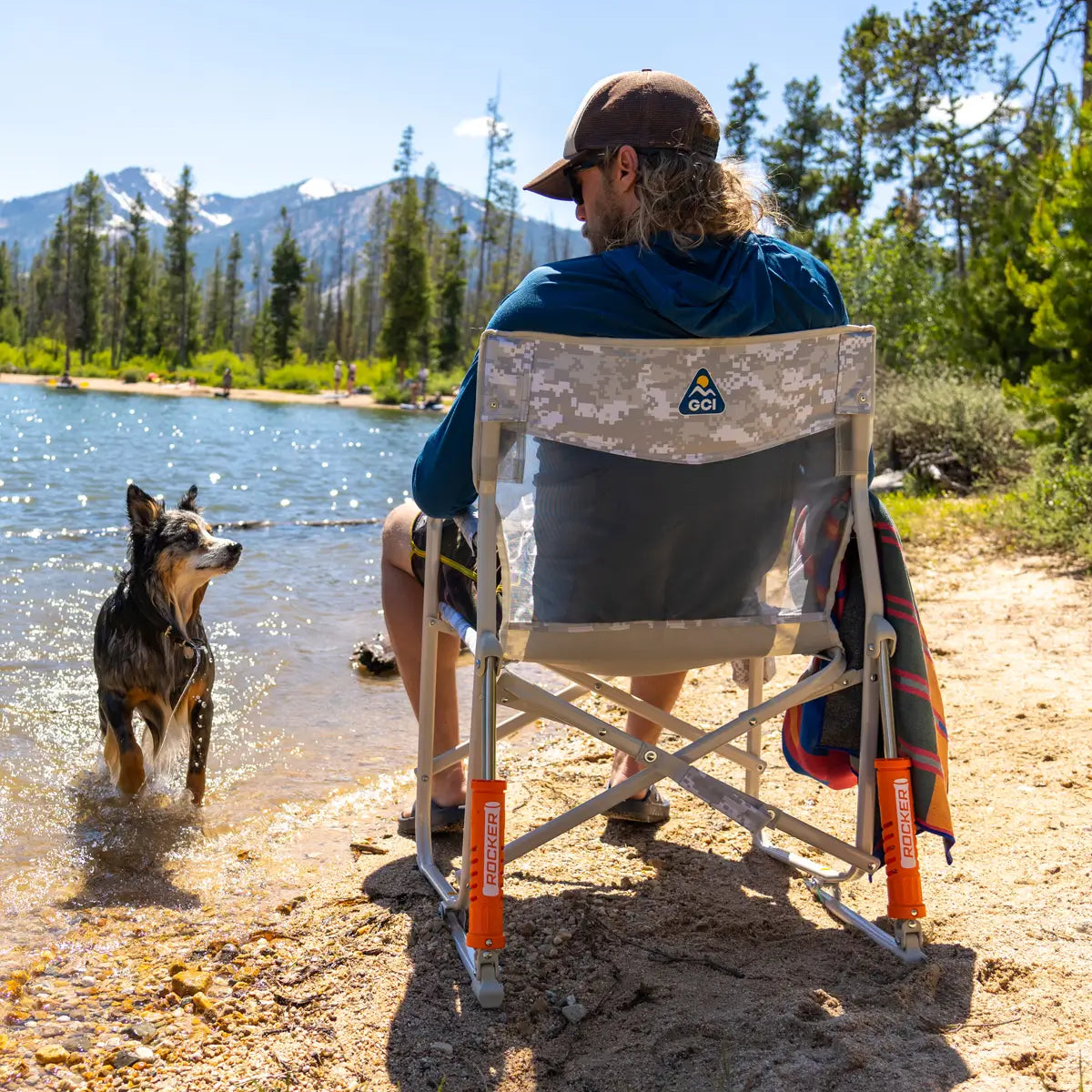 A man sitting in a Freestyle Rocker Elite chair next to a dog who is in a body of water. 