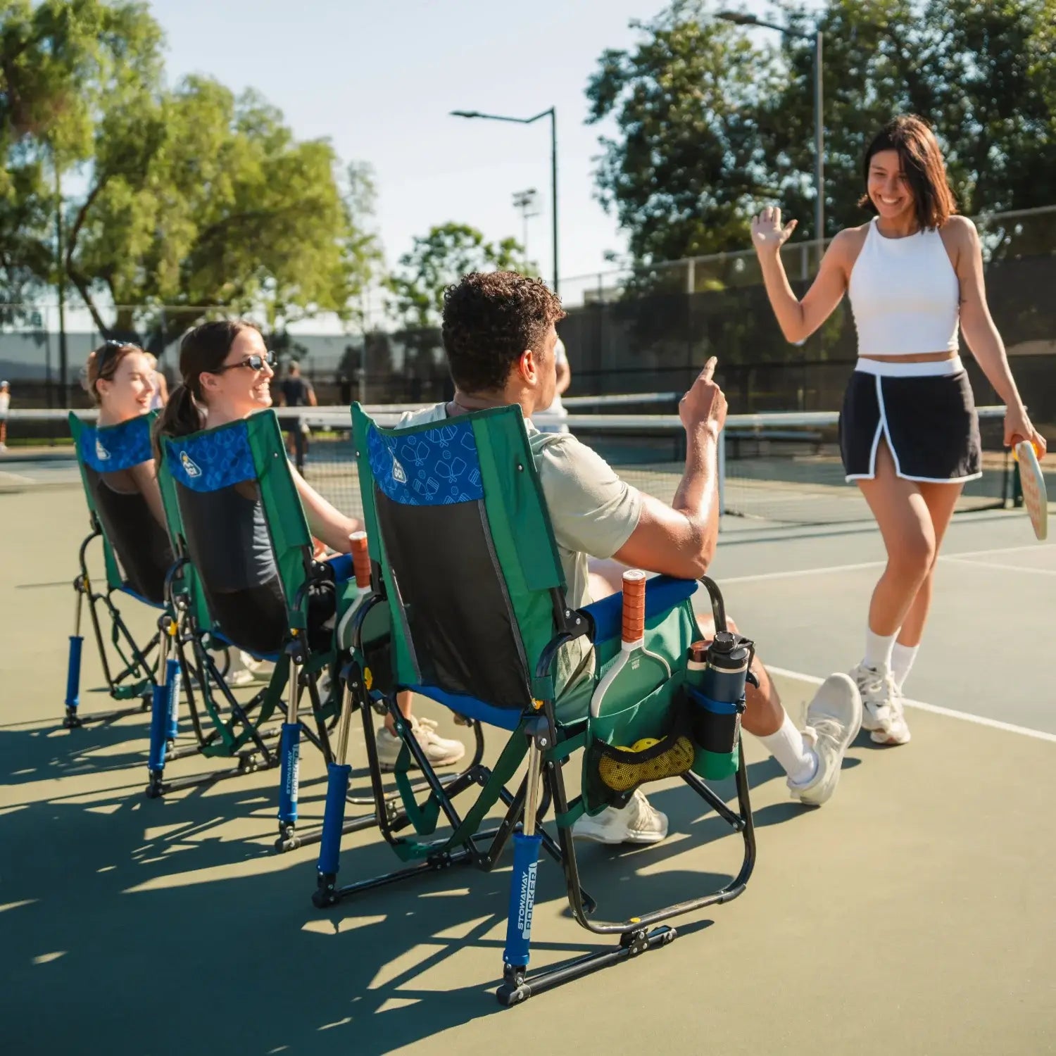 Three people sitting in a pickleball stowaway rocker while a woman high fives a man sitting.