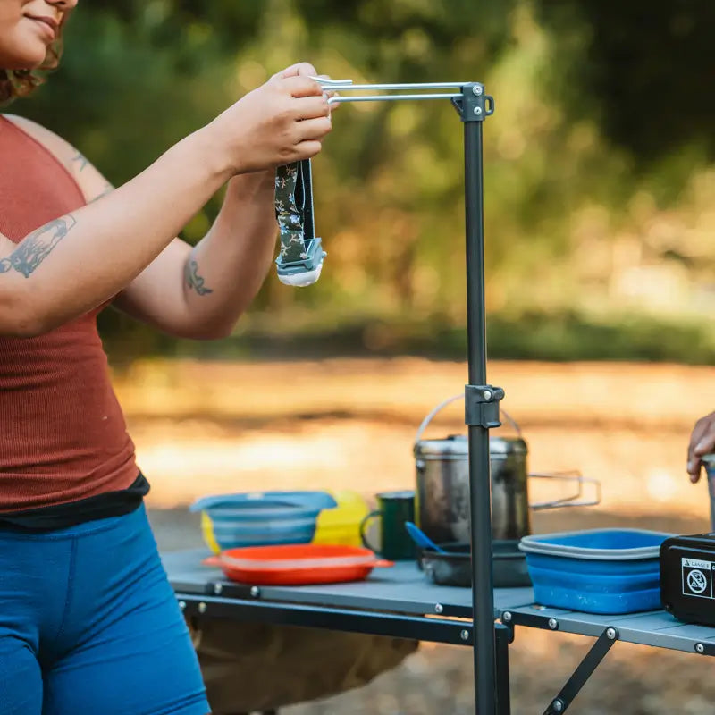 Camper hangs headlamp on lantern pole of master cook station during outdoor meal prep.