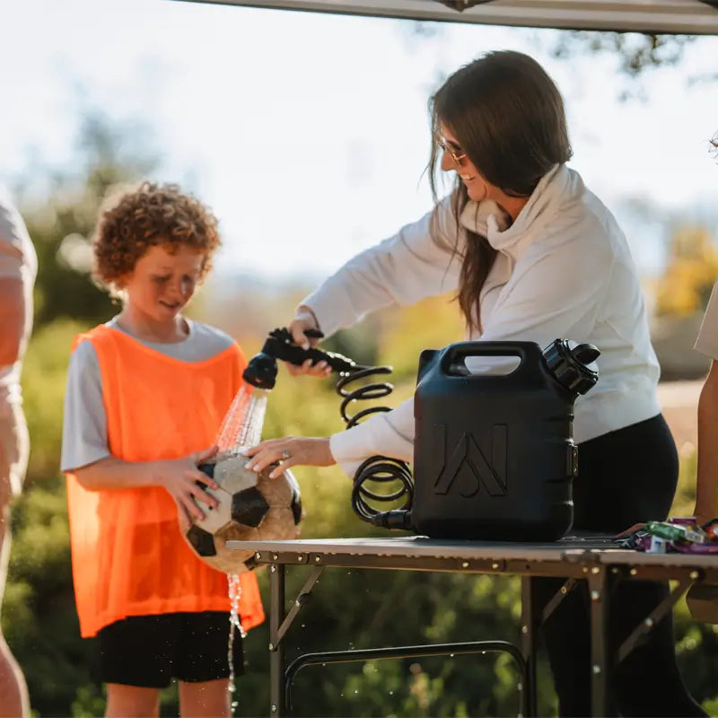 Woman using a portable sprayer on a soccer ball placed on a slim-fold table.