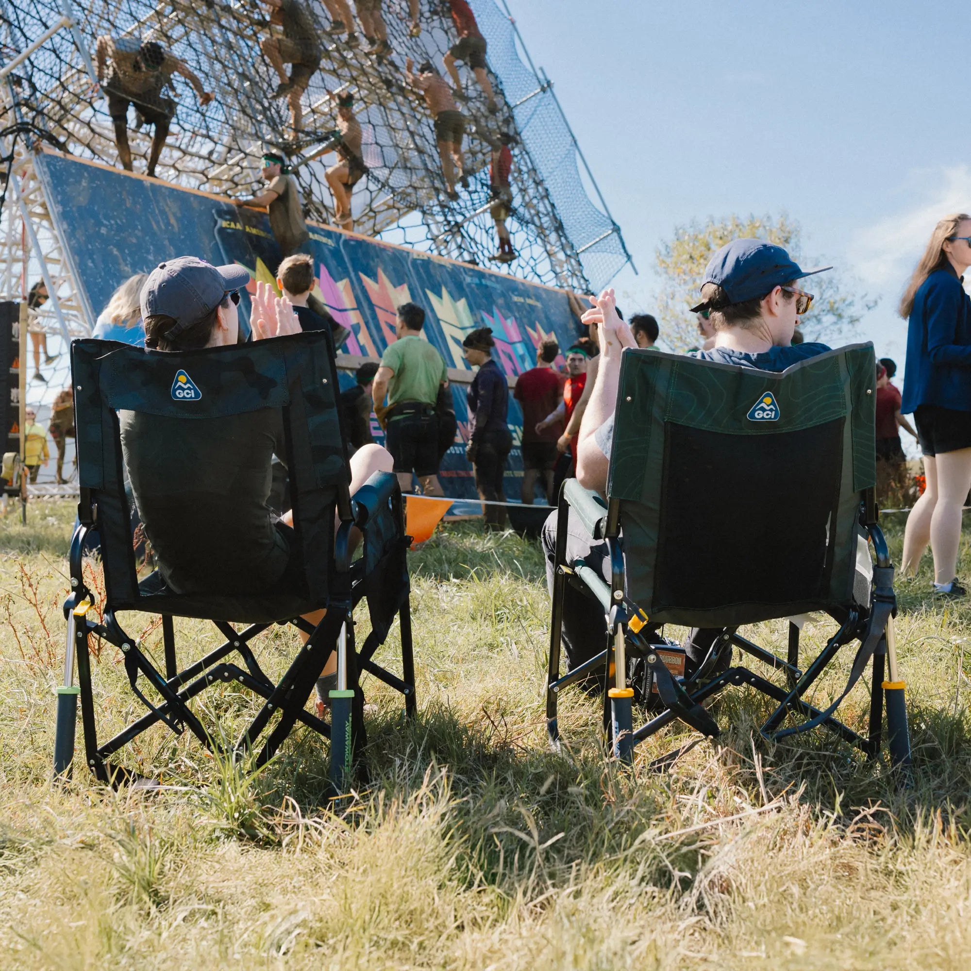 A couple sitting in stowaway rockers and clapping while watching people climb obstacles.