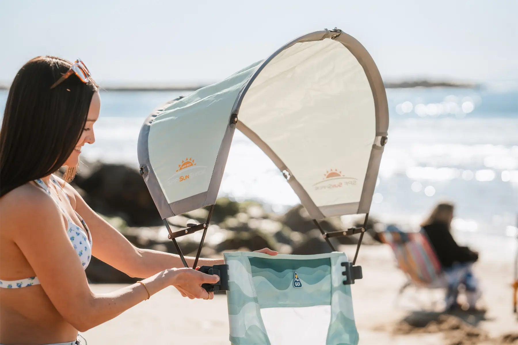 Woman adjusts canopy on a beach chair; close-up of the sunshade branded with “SunShade” and “GCI Outdoor.”