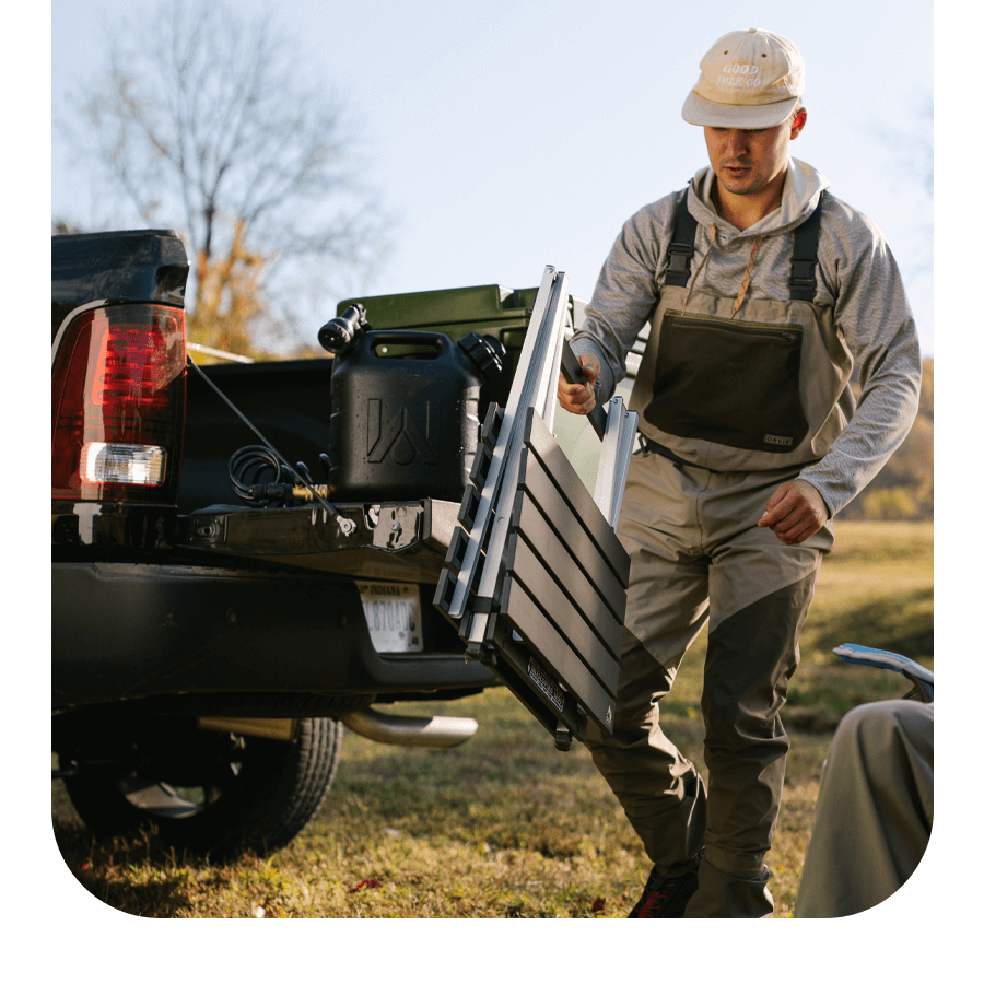 Man unloading a 168飞艇全国统一开奖结果查询官网 GCI Outdoor Compact Camp Table from a truck bed at a campsite.